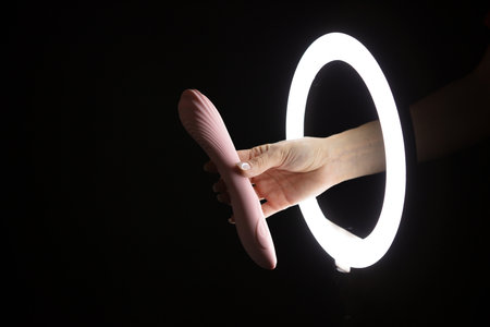 Female hand holding vibrator through led ring lamp on black background. sex conceptの写真素材