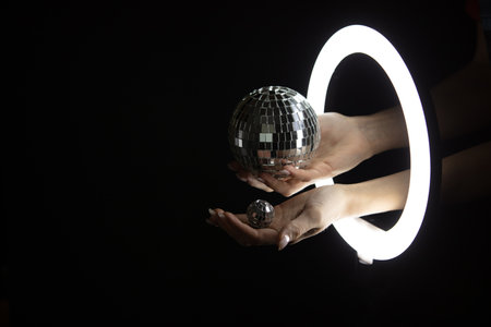 Female hands holding disco balls through led ring lamp on black background. party conceptの写真素材