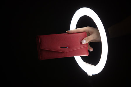Female hand holding leather wallet through led ring lamp on black background. fashion concept
