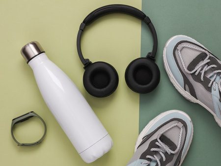 Fitness accessories on a green background. Thermos bottle, headphones, sneakers and smart bracelet. top viewの写真素材