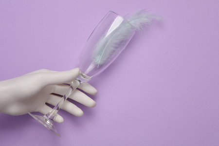 Hand holding Champagne glass with feather on a pastel background. top viewの写真素材