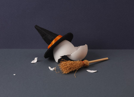 creative halloween layout. Eggshell and witch's hat, broom on dark background. concept pop. Minimal...