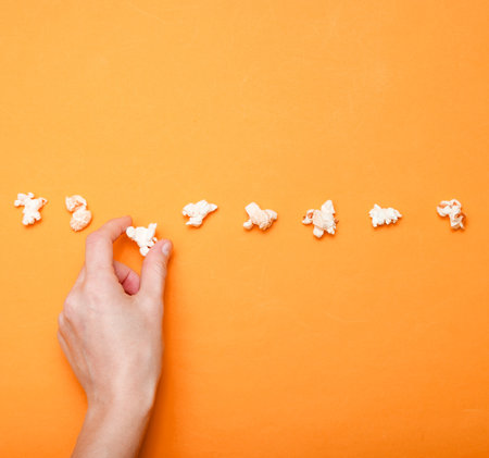 Popcorn line , hand takes popcorn on orange background. Minimalism, creative background. top view.の写真素材