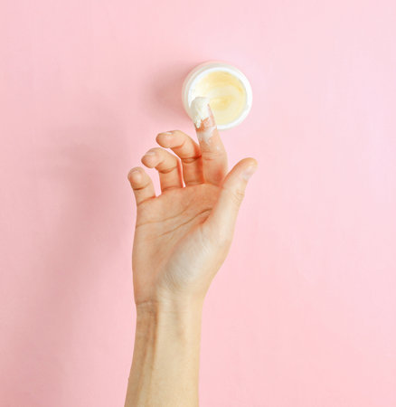 Female hand takes a moisturizing and softening cream for face skin on a pink background. minimalism.の写真素材