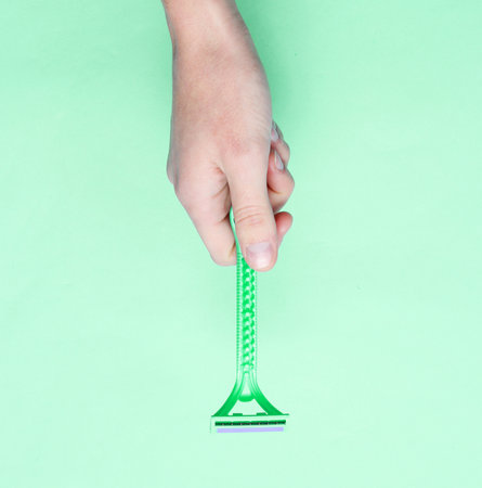 Female hand holding razors for epilation on green background. Top view, minimalism, flat lay styleの写真素材