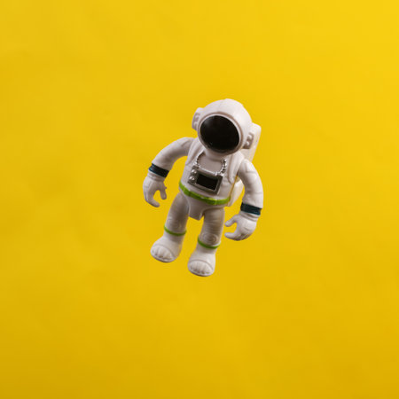 Toy astronaut model flying in antigravity on a yellow backgroundの写真素材