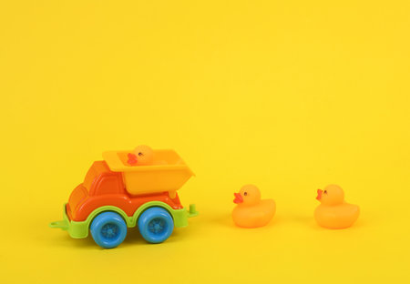 Toy dump truck with rubber little ducklings on a yellow backgroundの写真素材