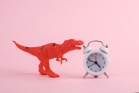 Toy dinosaur tyrannosaurus rex with alarm clock on pink background. minimalism creative layout