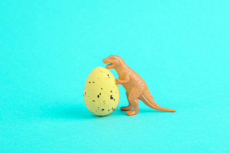 Toy dinosaur tyrannosaurus rex with easter colored egg on a turquoise background. minimalism creative layoutの写真素材