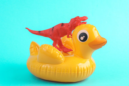 Toy red dinosaur tyrannosaurus rex with rubber duck on a turquoise background. minimalism creative...