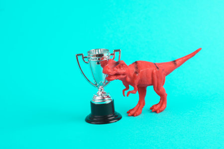 Toy red dinosaur tyrannosaurus rex with winner cup on turquoise background. minimalism creative layoutの写真素材