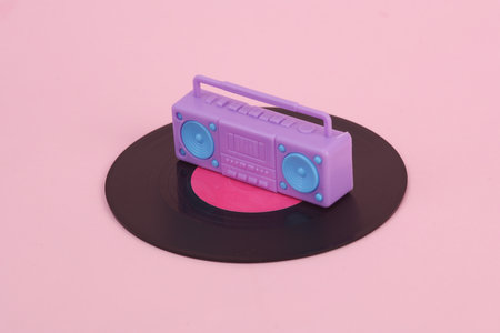 Plastic miniature boombox audio player and vinyl plate on pink background