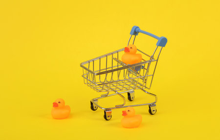 Rubber ducks with shopping trolley on yellow background. Niminimalism creative layoutの写真素材