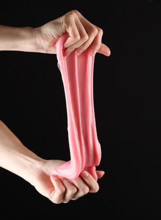 Female hands holding pink slime isolated on black background