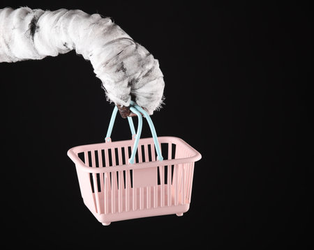 Mummy hand holding supermarket basket isolated on black background. Halloween, shoppinhg conceptの写真素材