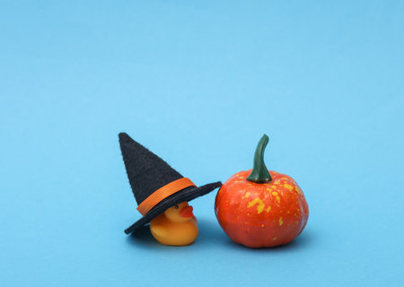 Halloween concept. Rubber duck with witch hat and pumpkin on blue background