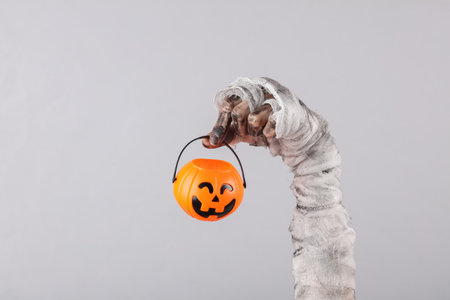 Mummy's hand wrapped in bandage holds halloween bucket isolated on gray background. halloween conceptの写真素材