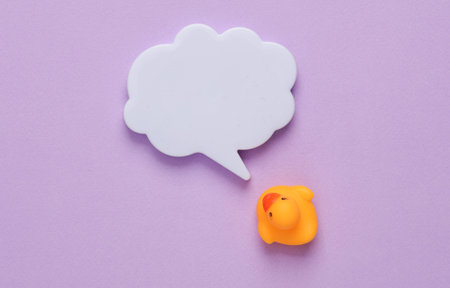 Rubber duck with empty speech bubble on purple background. top view