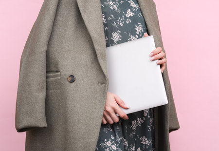 Woman in wool coat holding closed laptop on pink backgroundの写真素材