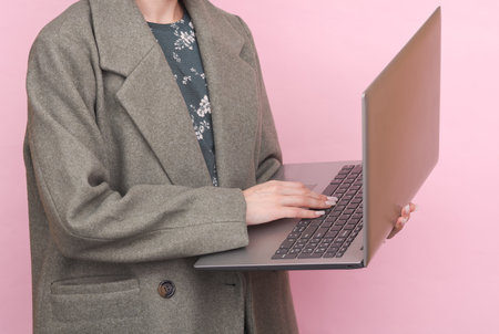 business woman in wool coat using laptop on pink backgroundの写真素材