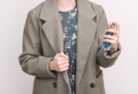 Fashionable woman in coat splashes herself with perfume on a white background. fashion conceptの写真素材