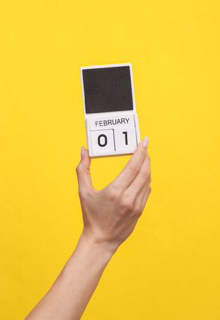 Female hand holding wooden calendar with date February 01 on yellow backgroundの写真素材