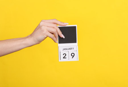Female hand holding wooden calendar with date January 29 on yellow backgroundの写真素材