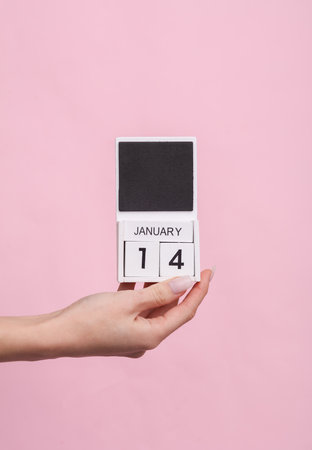 Female hand holding wooden calendar with date January 14 on pink backgroundの写真素材