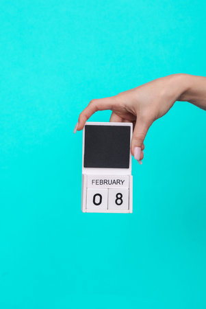 Female hand holding wooden calendar with date February 08 on blue backgroundの写真素材