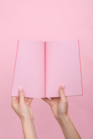 Female hands hold a notepad with pink sheets of paper on a pink pastel background.の写真素材