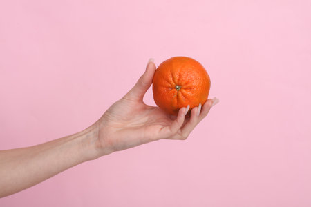 Woman's hand holding a tangerine on a pink backgroundの写真素材