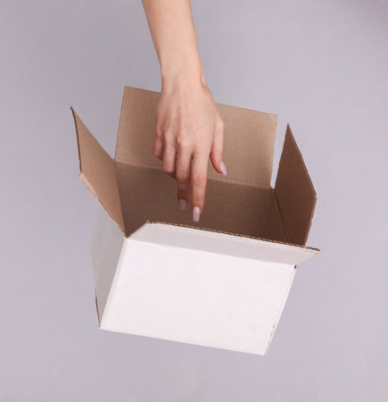 Open cardboard box and female hand on gray backgroundの写真素材