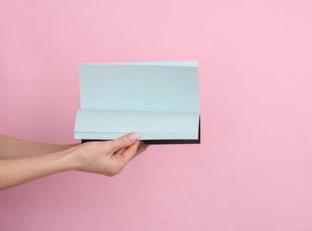 Female hands hold a notepad with blue sheets of paper on a pink pastel background.の写真素材