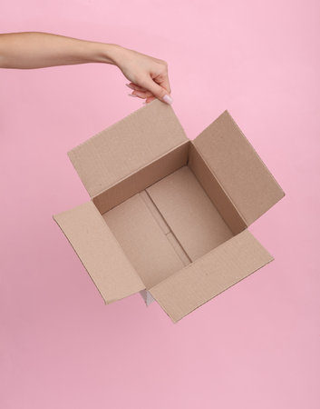 Empty cardboard box in a female hand on a pink backgroundの写真素材