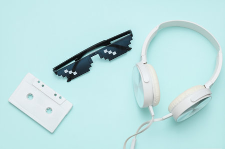 Stereo headphones with Pixelated 8 bit sunglasses and audio cassette on blue pastel backgroundの写真素材
