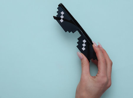 Woman's hand holding pixel glasses on blue background