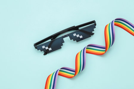 Pixelated 8 bit sunglasses with lgbt rainbow ribbon on blue pastel background