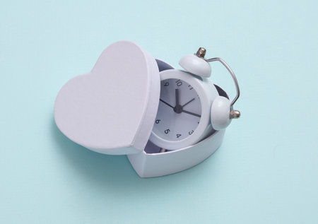 Alarm clock in a box in the shape of a heart on a blue background. love concept. Valentine's Day