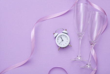 New Year celebration. Glasses with an alarm clock and a satin ribbon on a lavender background....