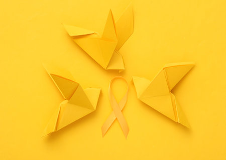 Yellow childhood cancer awareness ribbon and origami doves on yellow backgroundの写真素材