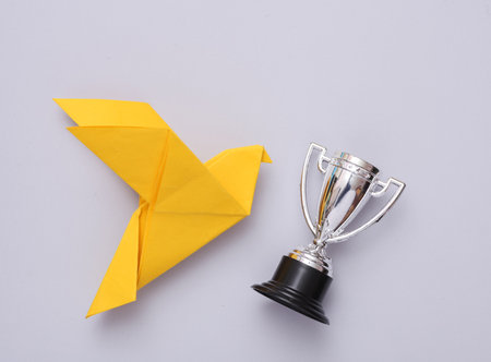 Origami dove with winner cup on a gray background.