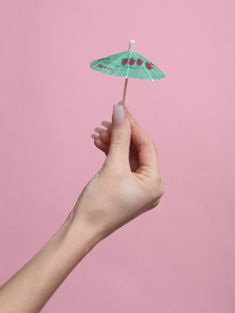 Woman's hand holding a cocktail umbrella on a pink backgroundの写真素材
