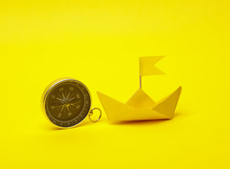 Leadership, pursuit of goals, navigation, business concept. Paper boat and compass on yellow backgroundの写真素材