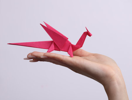 Female hand holds origami Dragon on white background. Hobby, creativityの写真素材