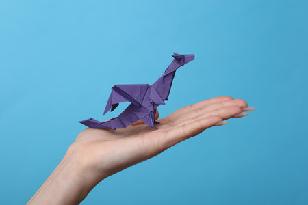 Female hand holds origami Dragon on blue background. Hobby, creativityの写真素材