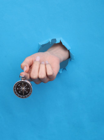 Female hand holds compass through torn hole of blue paperの写真素材