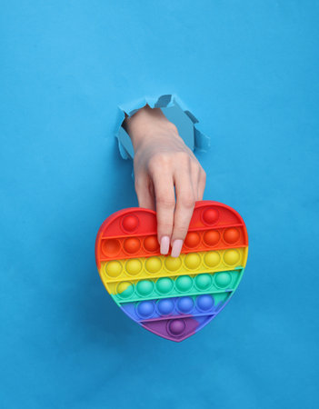 Female hand holds pop it antistress toy through torn hole of blue paperの写真素材