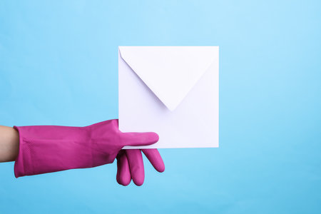 Hands in purple rubber cleaning gloves holding envelope on blue background.