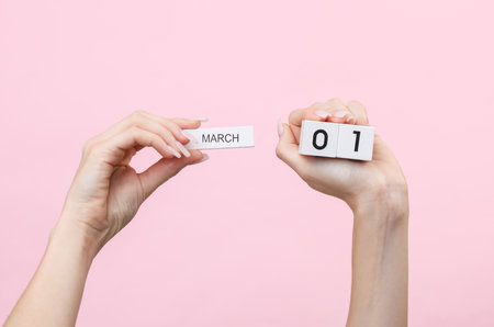 Woman's hands hold wooden block calendar with the date 01 march on pink background