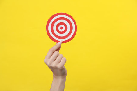 Hand holding a target on a yellow background. business concept